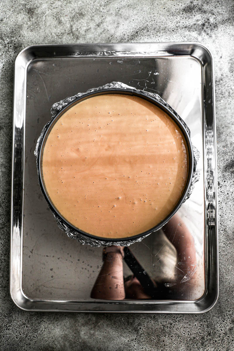 El relleno del cheesecake de dulce de leche dentro del molde forrado con papel de aluminio sobre una fuente para horno.