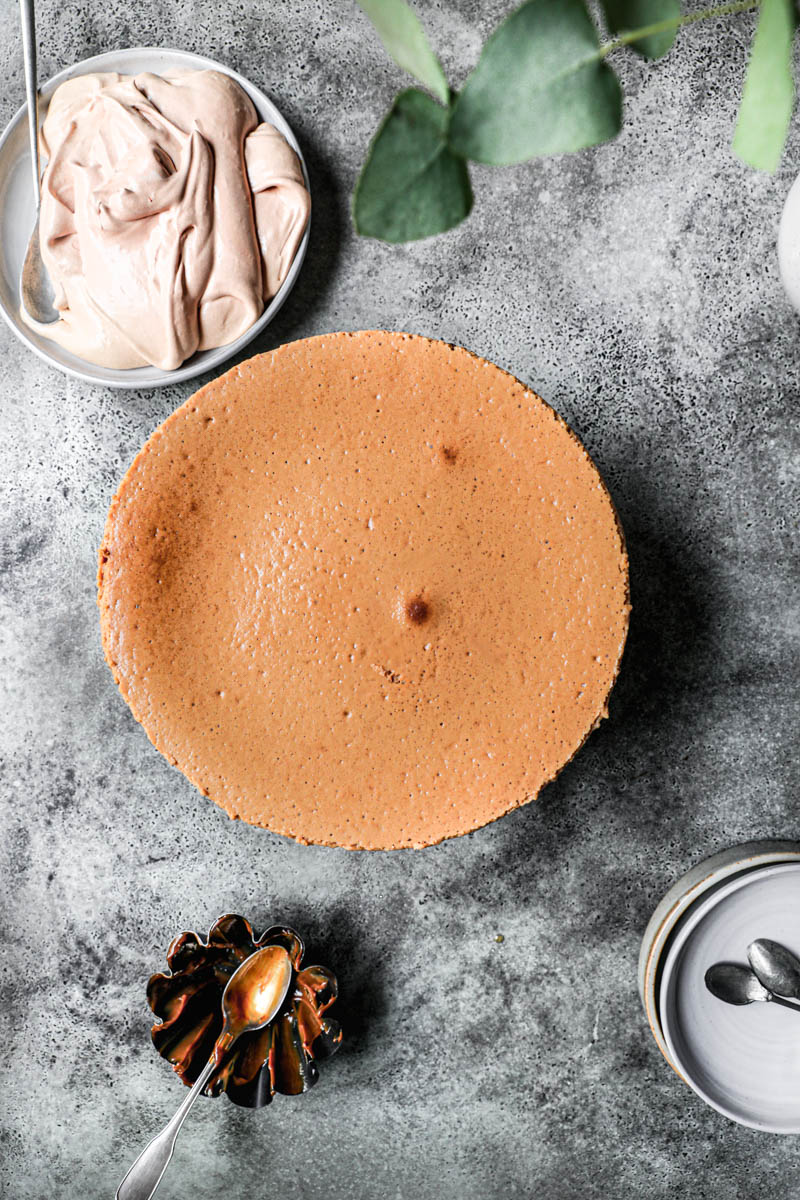 El cheesecake horneado visto desde arriba con un plato a su lado relleno de crema de dulce de leche.