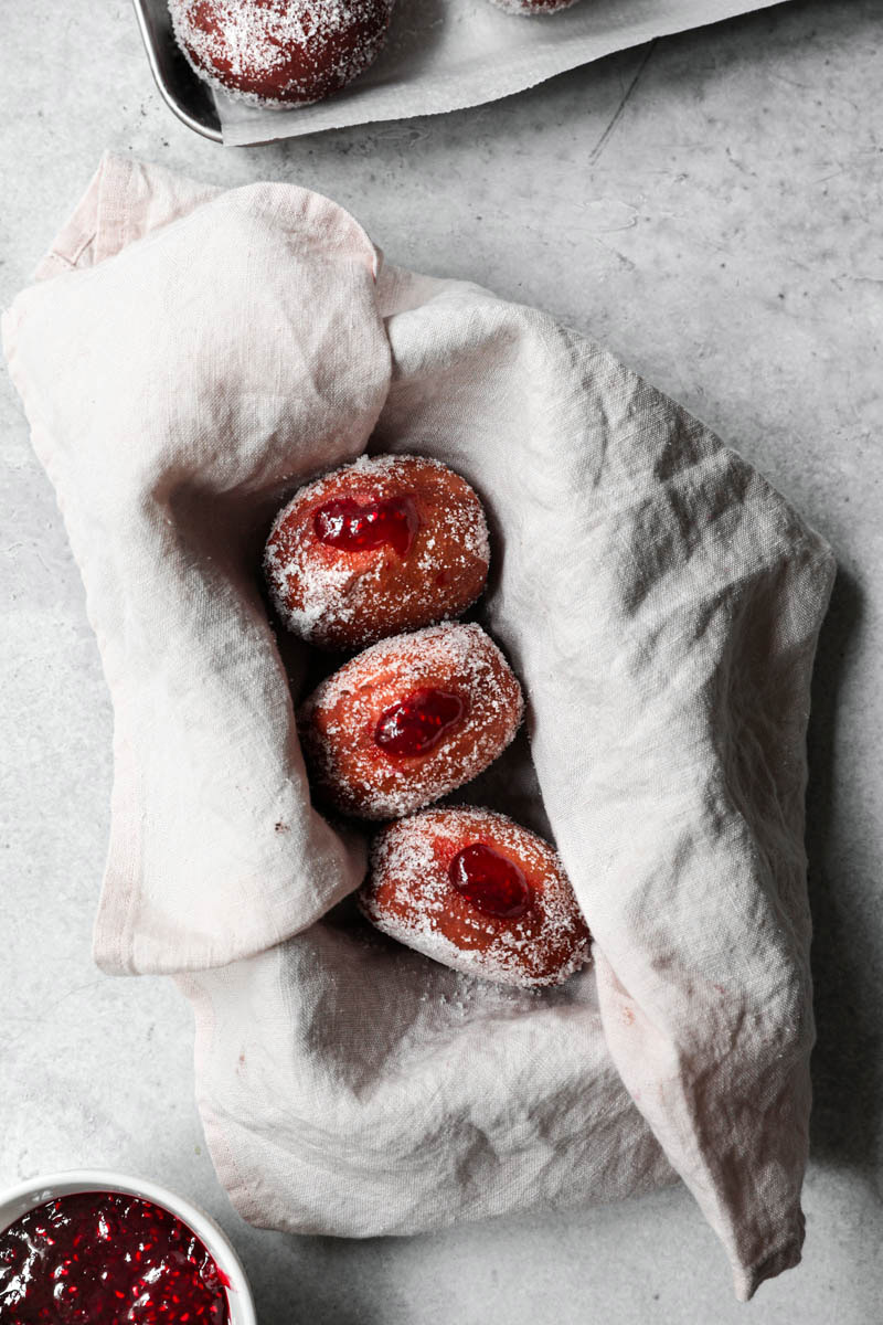 3 donuts rellenos de mermelada de frambuesa dentro de un molde rectangular forrado con una servilleta de lino rosa.