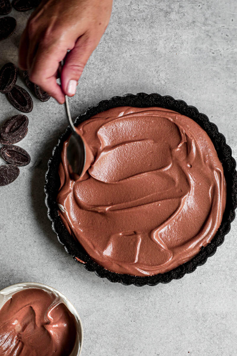 Plano aéreo de una mano esparciendo la mousse de chocolate sobre el fondo de la tarta usando una cuchara
