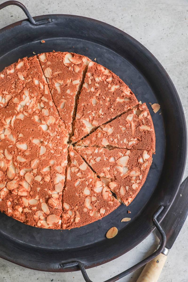 The sliced almond cake on a black tray with a knife on the side.