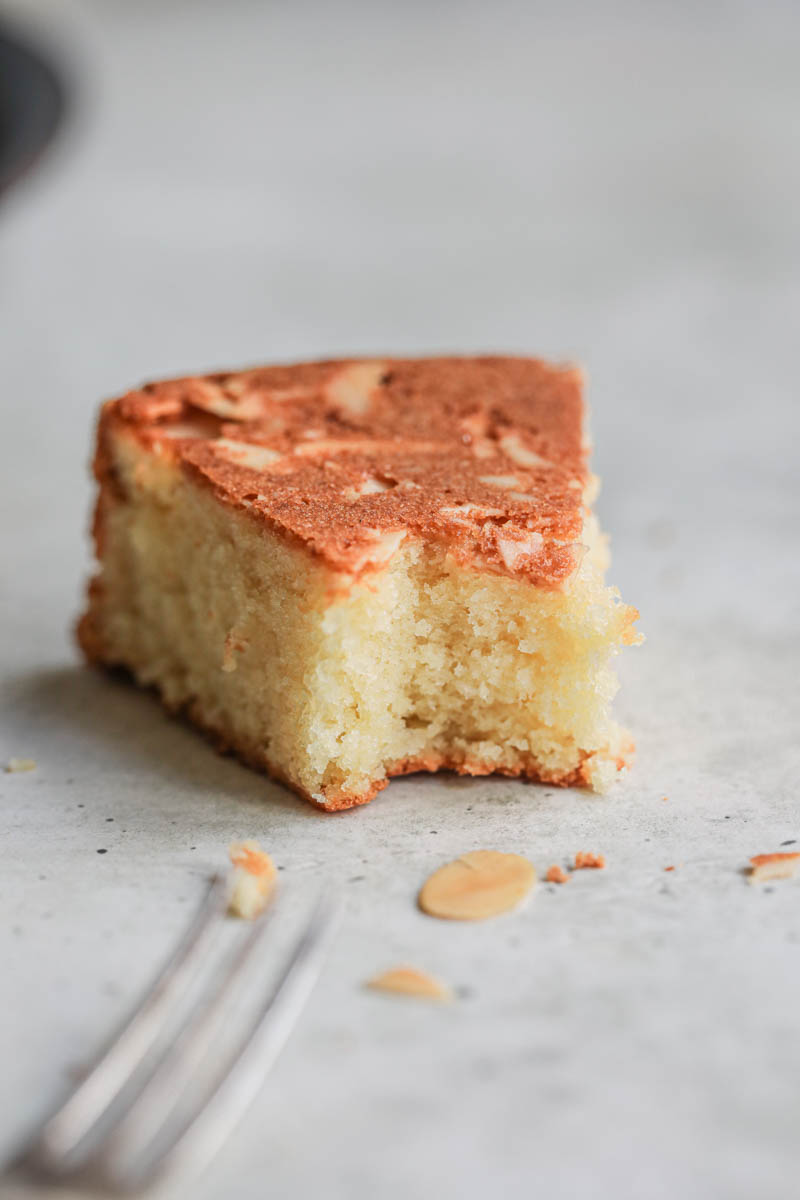 A closeup of one slice of almond paste cake with a fork on the bottom left of the frame.