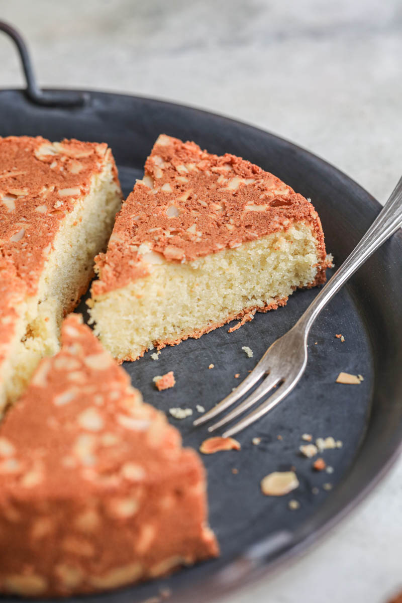 The almond paste cake sliced on the black tray with a spoon on the side.