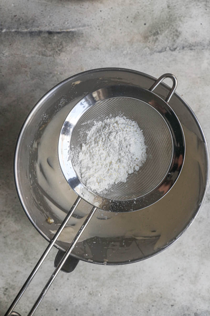 Sifting the dry elements inside a strainer over the almond cake batter.