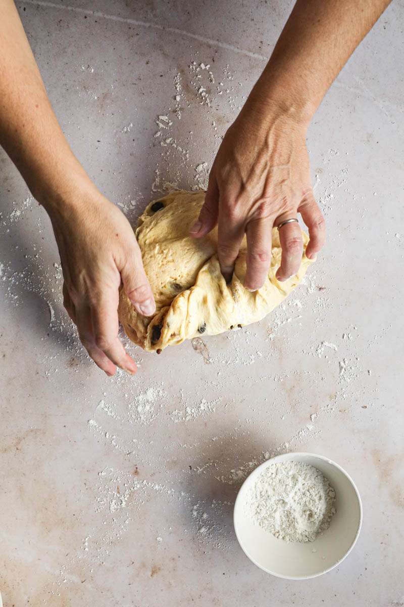 Two hands shaping the Kugelhopf bread dough and a small bowl with flour on the bottom side of the frame.