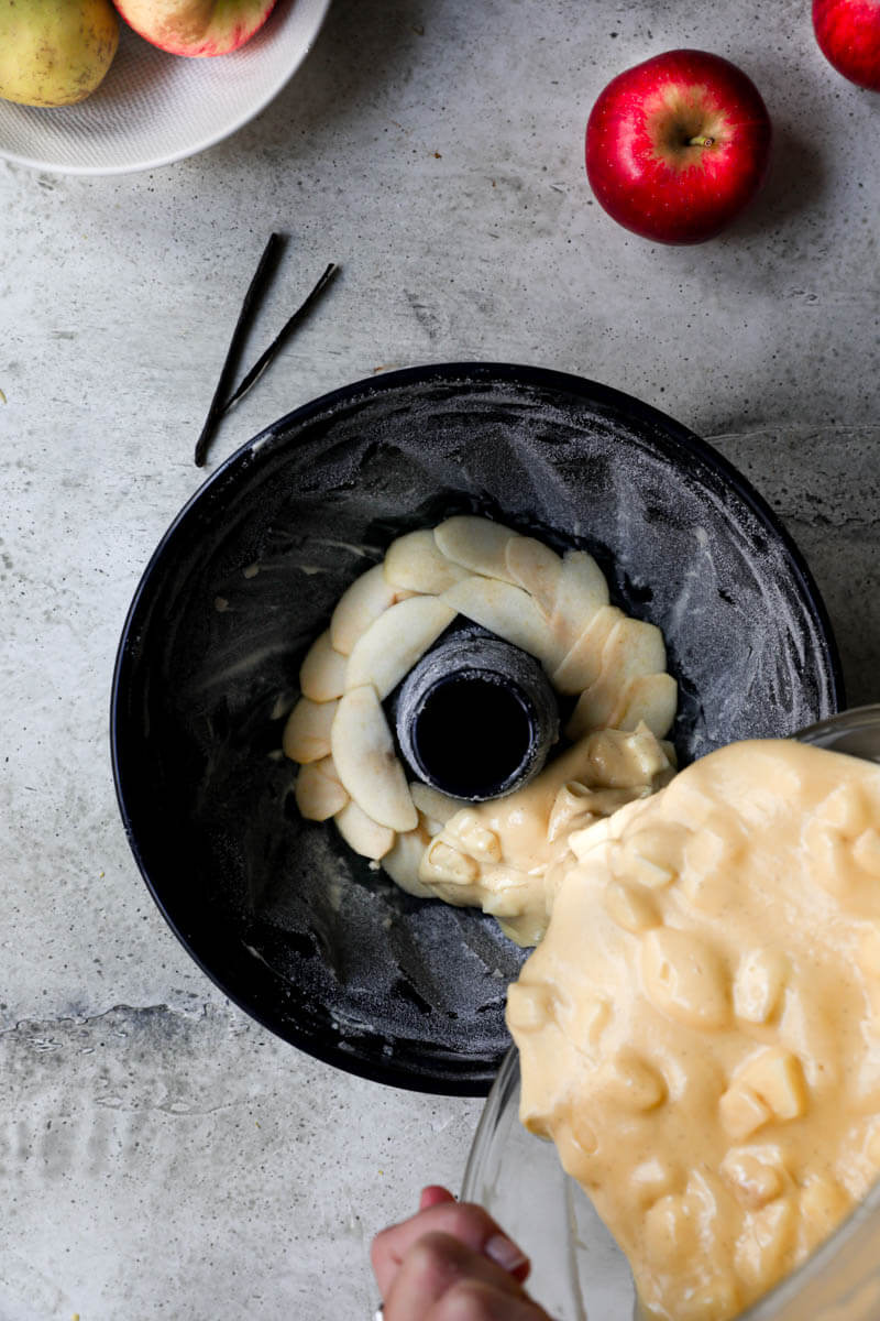 Overhead shot of a hand filling the cake pan with the apple cake batter