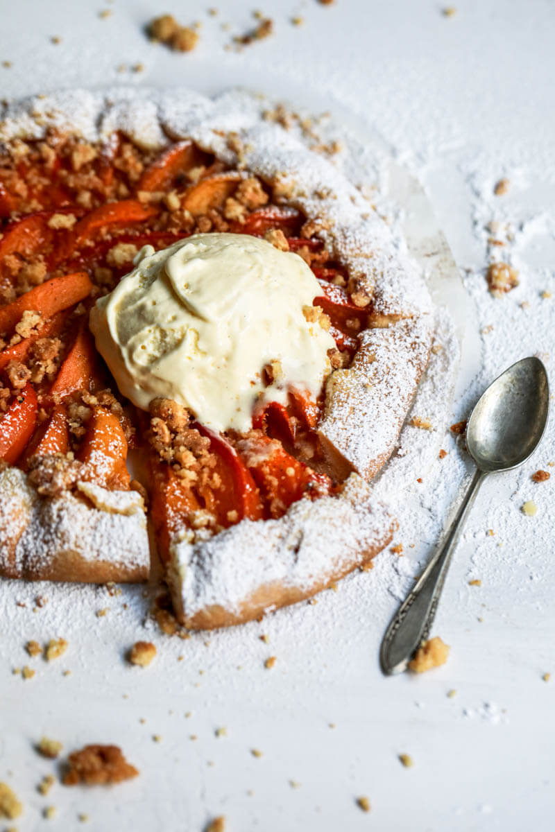 45° shot of the baked apricot tart with a sliced portion and a scoop of vanilla ice cream on top.