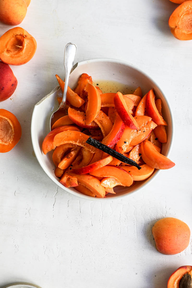 Overhead shot of sliced apricot in a bowl mixed with vanilla and orange juice.