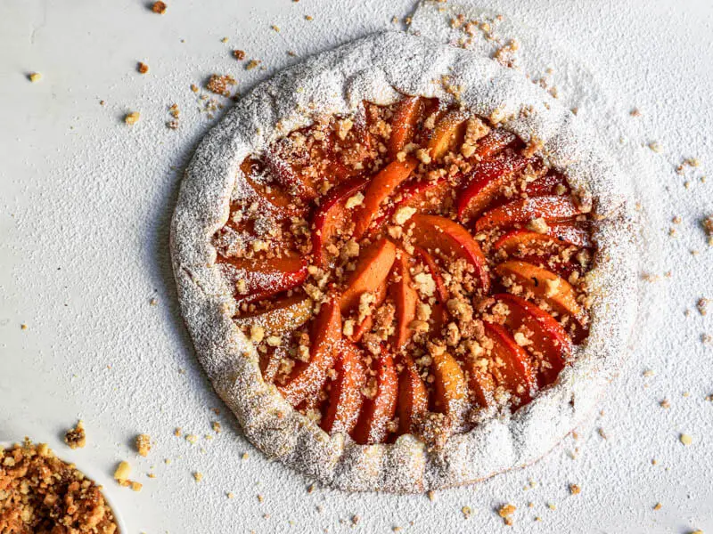 Overhead shot of the baked apricot tart topped with hazelnut crumble and sprinkled with powdered sugar.