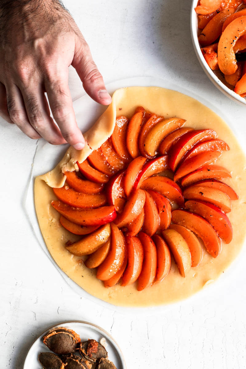 Overhead shot of the crust filled with the sliced apricots and a hand folding over the dough.