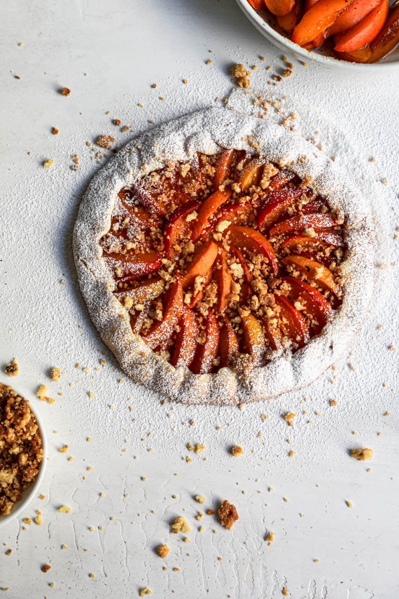 Overhead shot of the baked apricot tart topped with hazelnut crumble and sprinkled with powdered sugar.