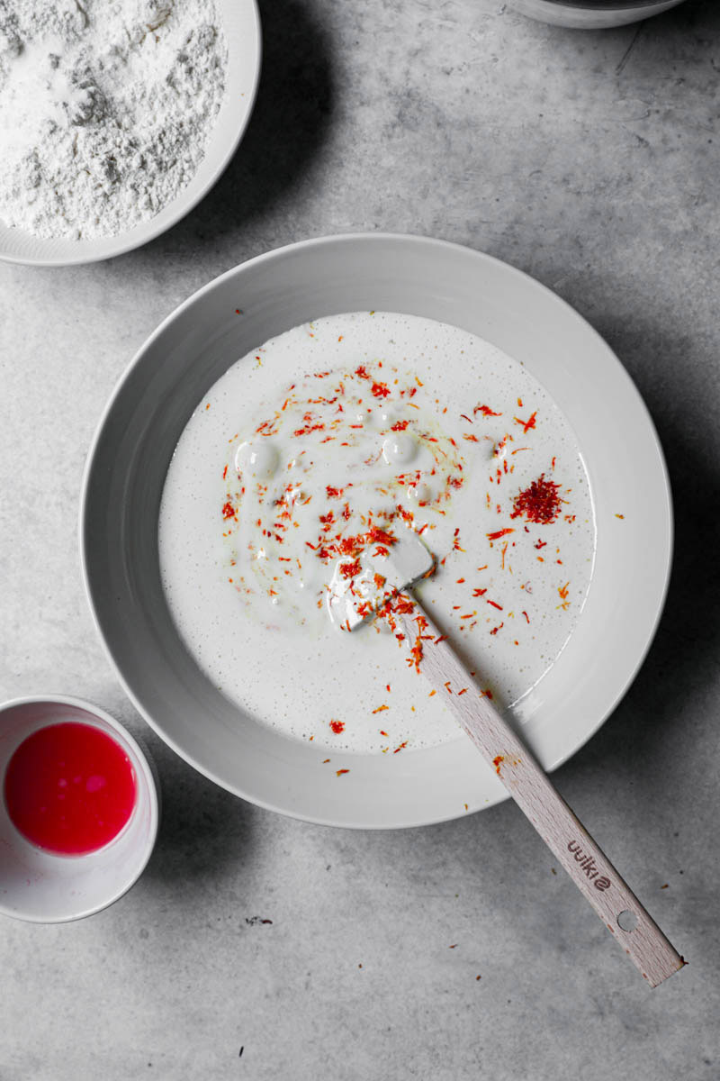 Blanched eggs and sugar plus blood orange zest in a white bowl.