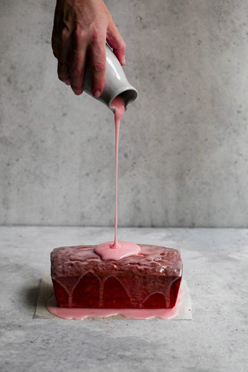 One hand pouring over the blood orange glaze on the blood orange pound cake.