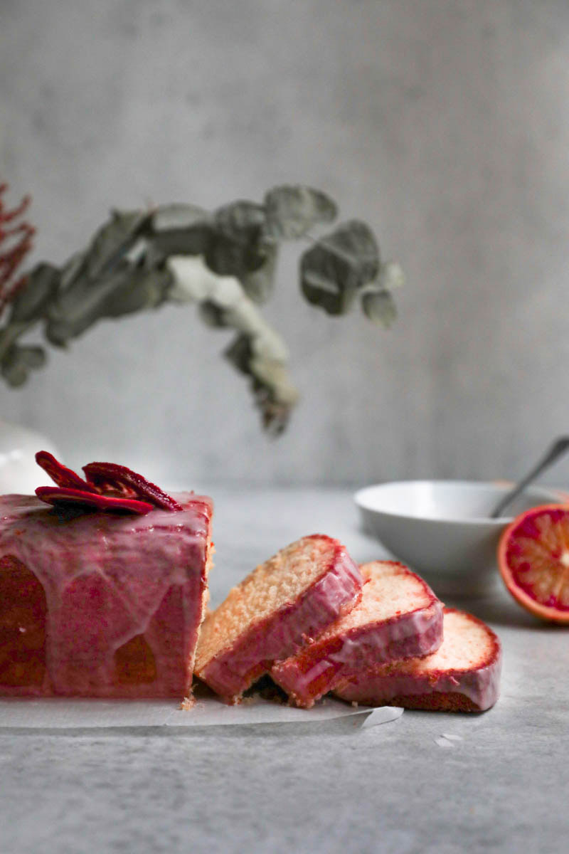 Sliced blood orange cake seen from the side with some leaves in the back and jar on the side.