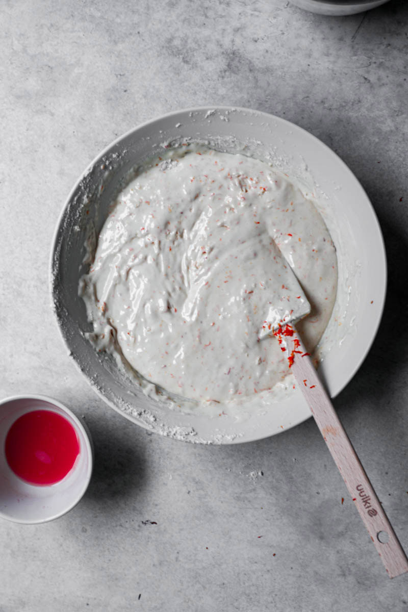 Blood orange cake batter in the making inside a white bowl with the juice on the side.