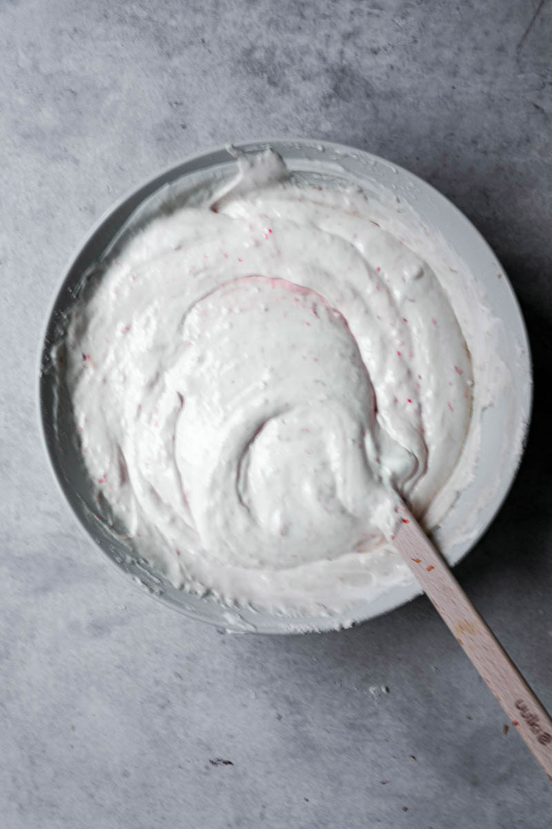 Blood orange cake batter ready inside a white bowl with a wooden spatula on the side.