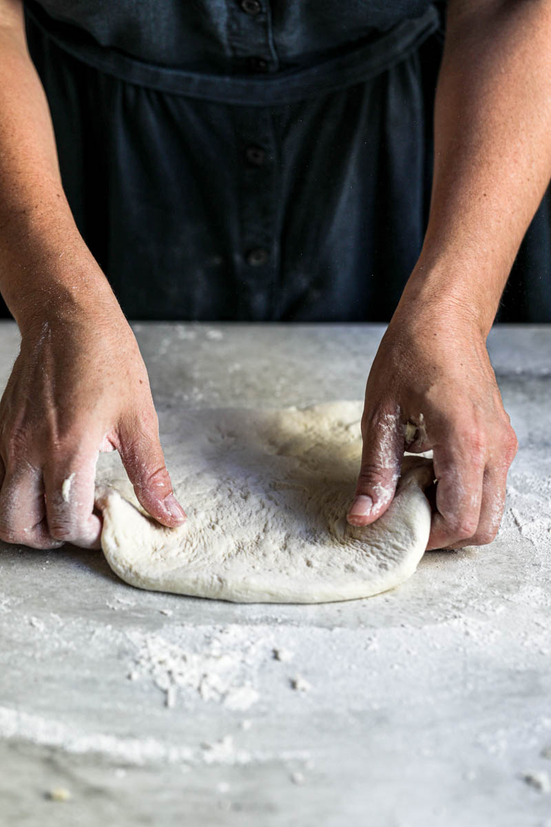 2 hands relaxing the pizza dough before stretching