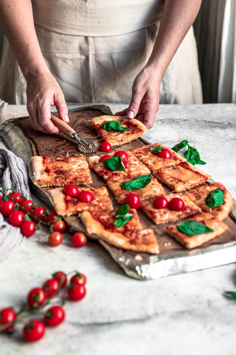 45° shot of 2 hands holding a slice of the baked margherita pizza on a wooden board