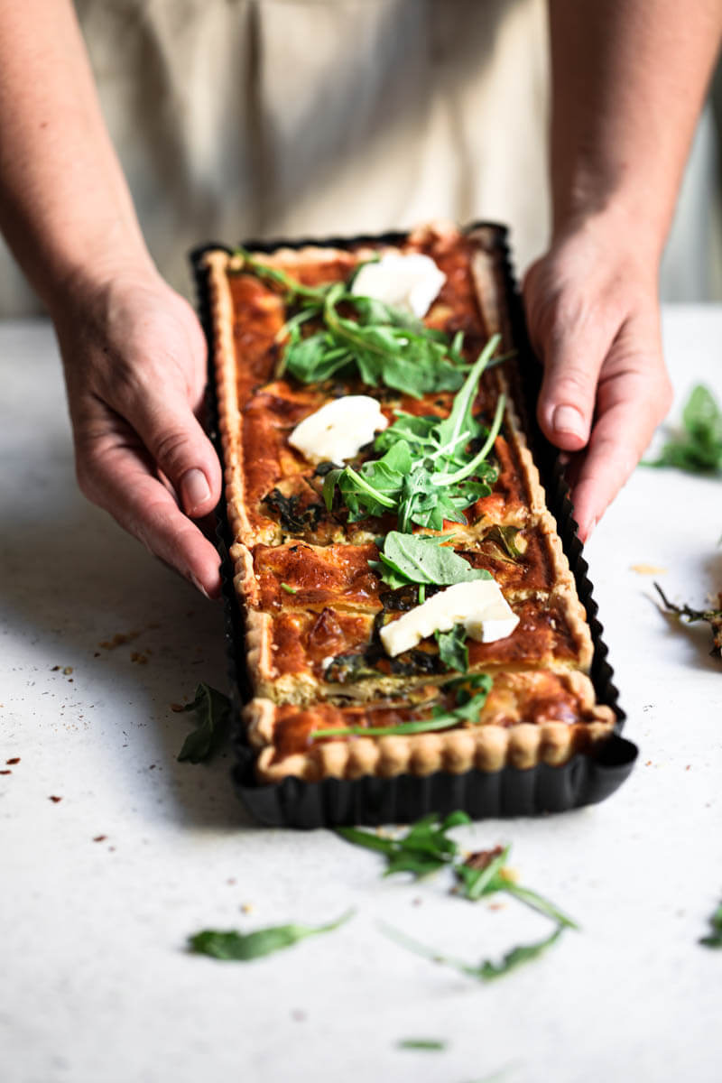 45° shot of 2 hands holding the brie caramelized onion quiche in the quiche tin