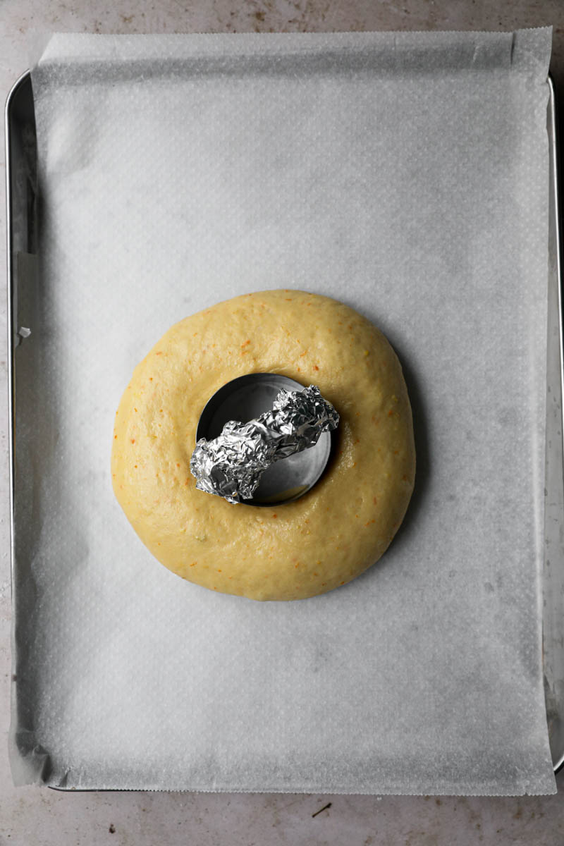 Easter bread with a whole in the middle and small cutter placed inside on a baking tray lined with parchment paper.