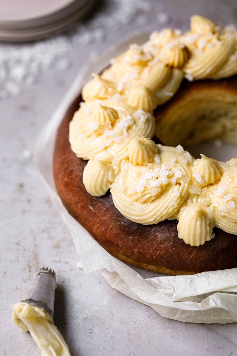 The Easter bread topped with pastry cream with plates on the background and a piping tip on the left bottom corner.