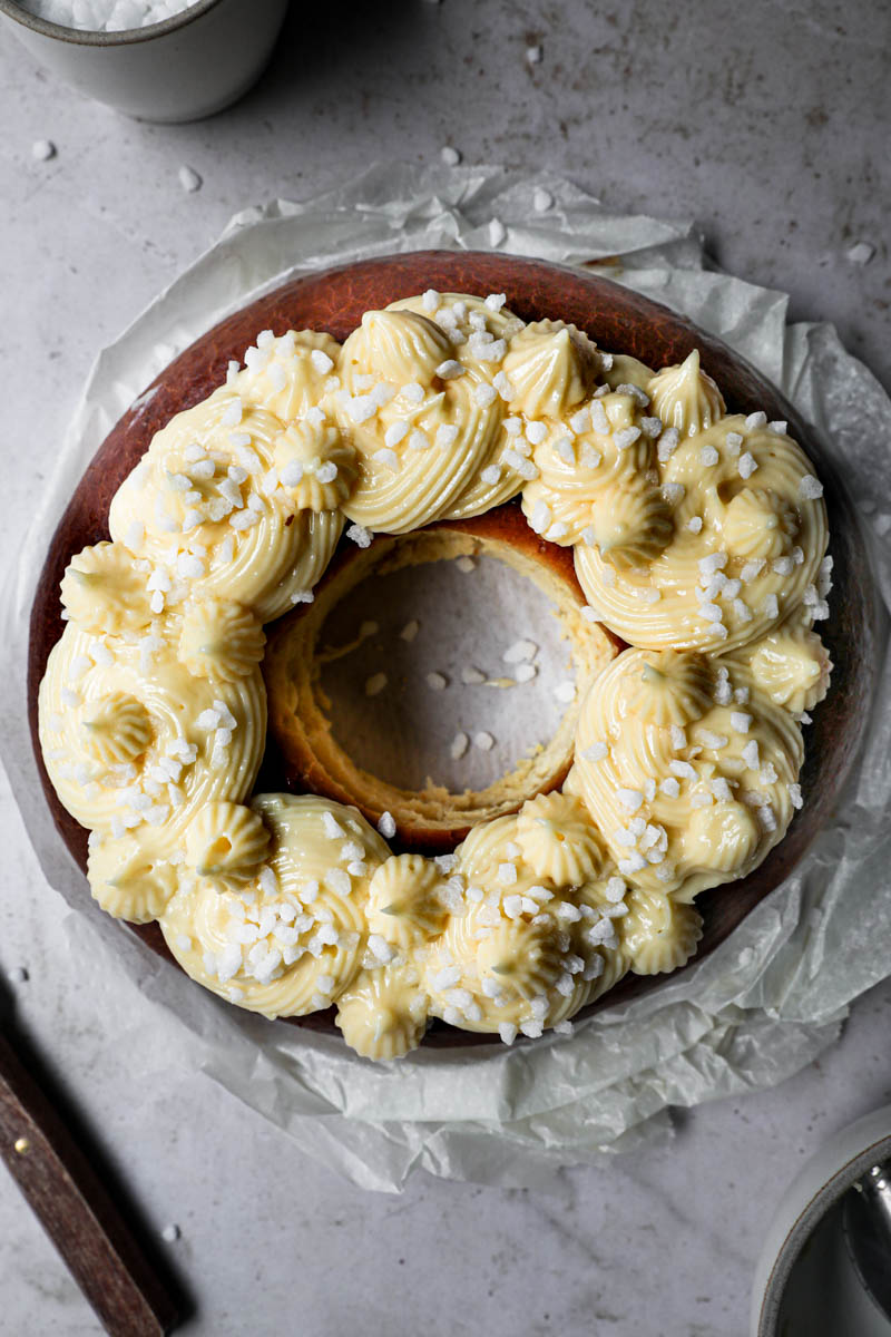 Easter bread topped with homemade pastry cream and pearl sugar with a bowl in the top left corner and a knife on the bottom left corner.