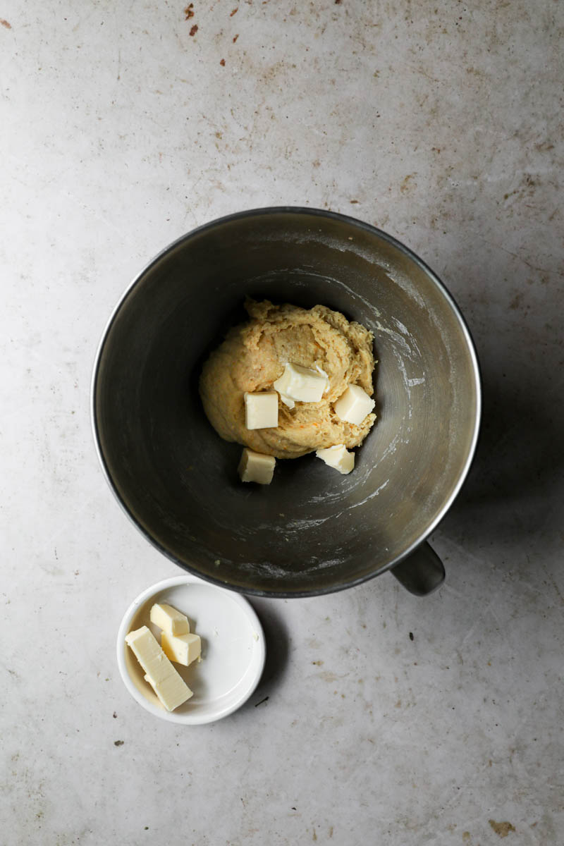 The kneaded dough plus half of the softened butter inside a bowl.