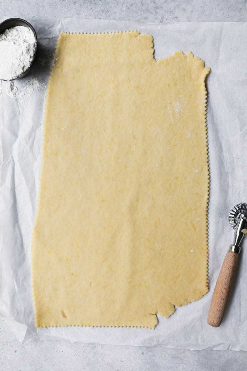 The bugnes dough thinly rolled on a piece of parchment paper with a pasta wheel on the side