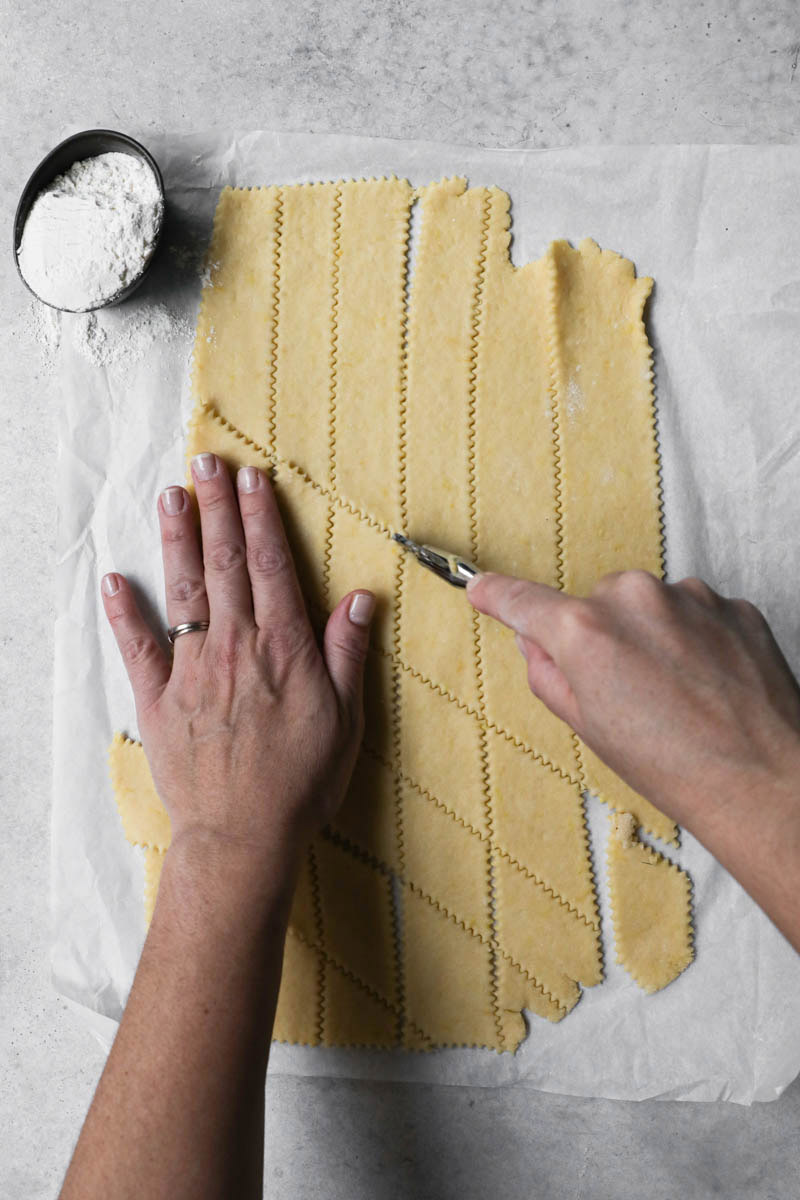 A hand cutting the bugnes using a pasta wheel cutter