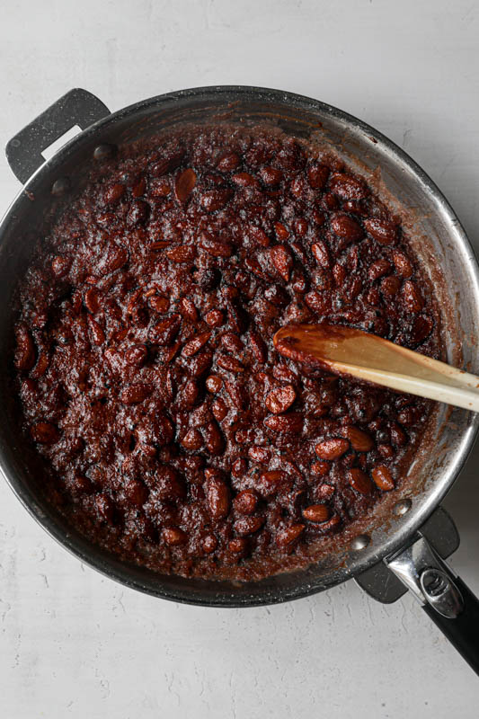 The caramelized almonds, the sugar and the water inside a pan with a spatula on the side.