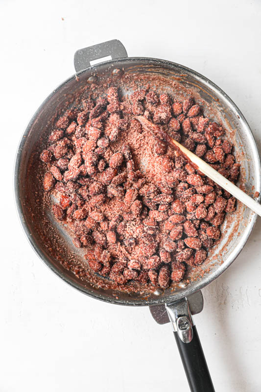 The almonds coated with a white sandy caramel inside a pan.