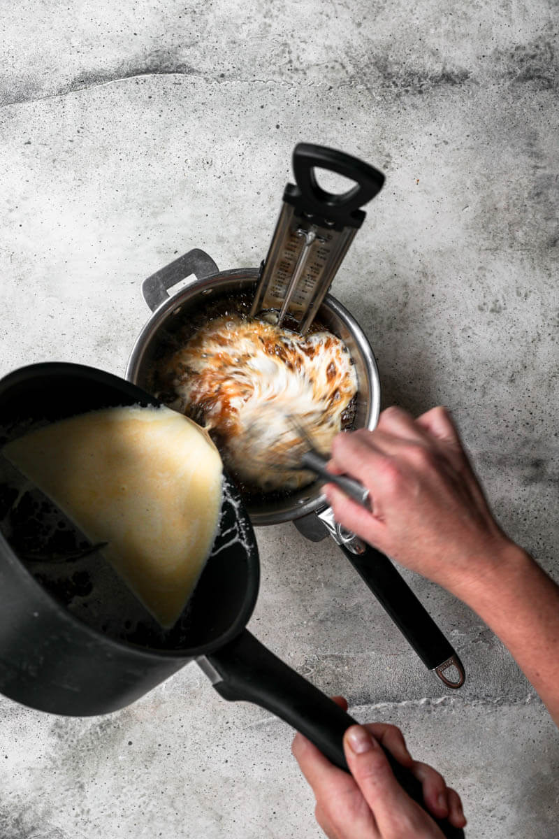 One hand pouring cream and butter over a pan with caramel