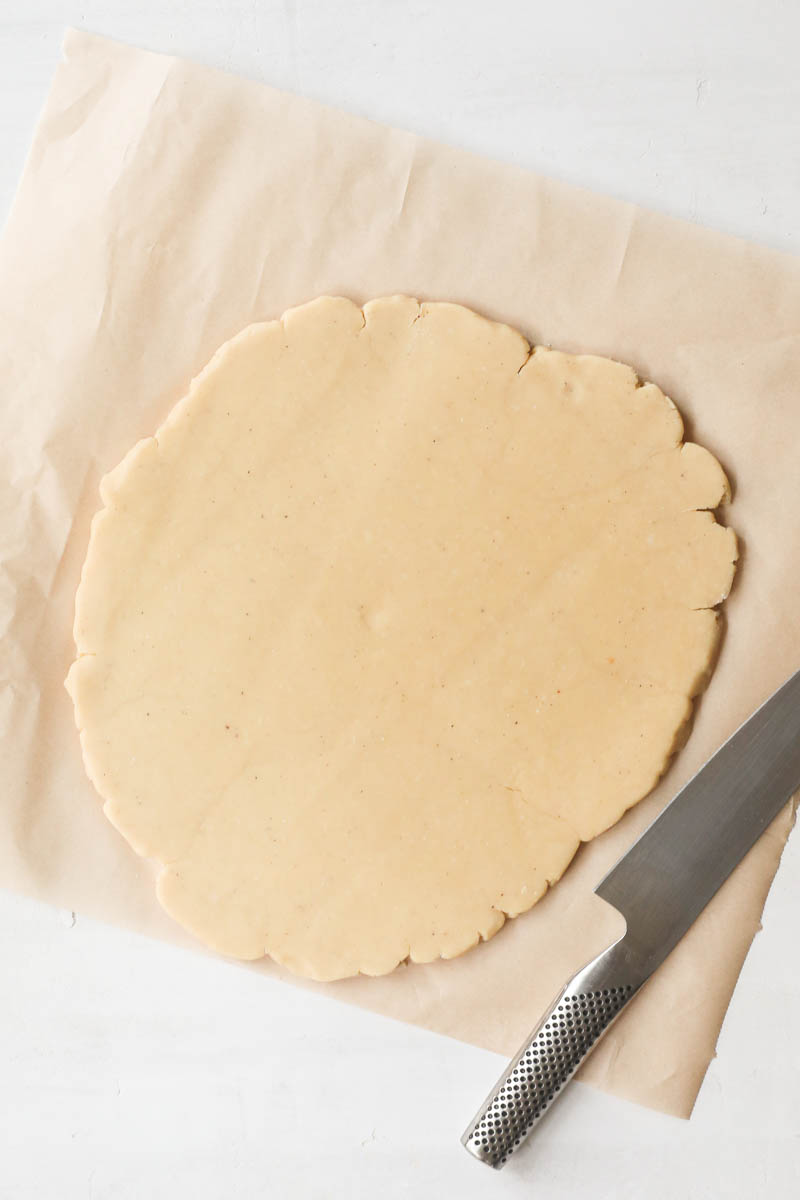 The rolled out parmesan cheese cookie dough over a parchment paper with a knife on the side.