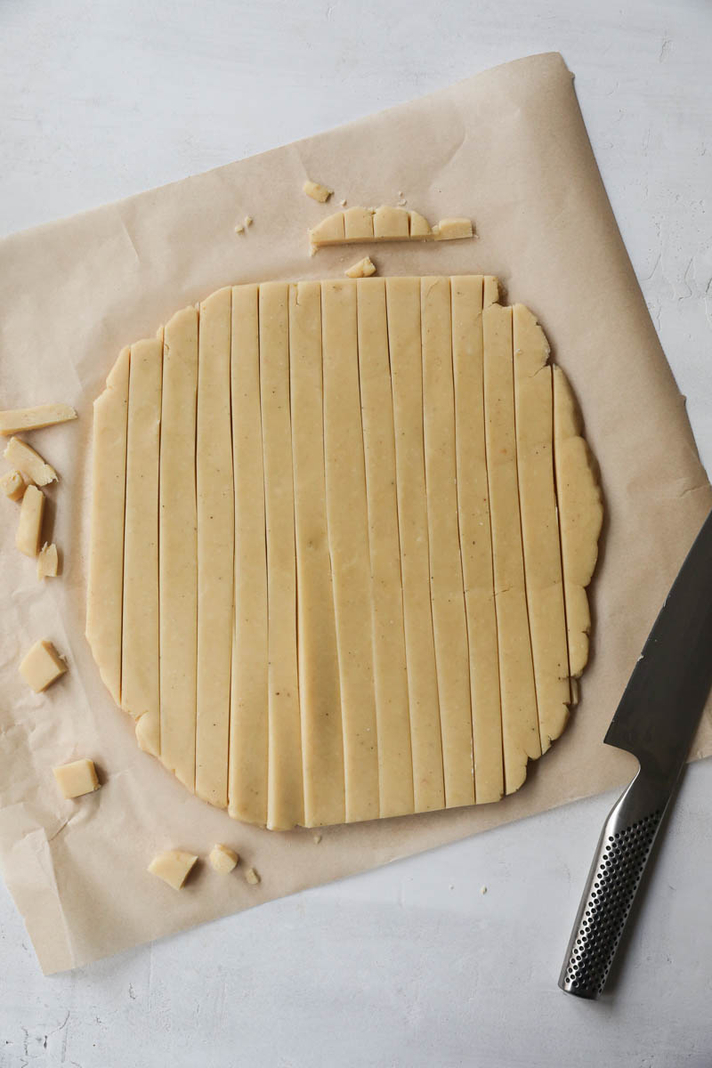 The rolled out parmesan cheese cookie dough over a parchment paper cut into strips.