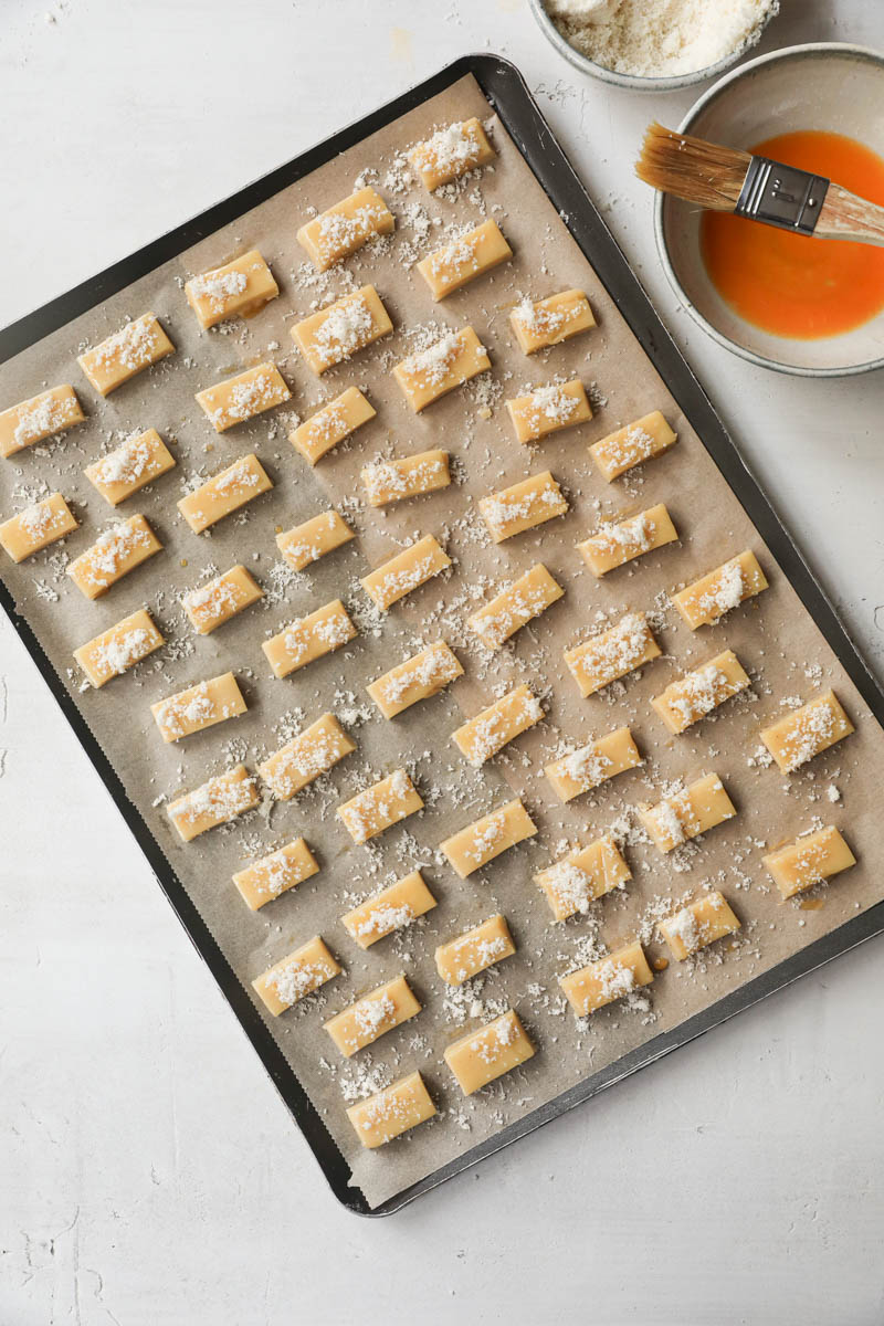 The parmesan cheese cookies placed on a baking tray lined with parchment paper brushed with egg wash and sprinkled with parmesan cheese.