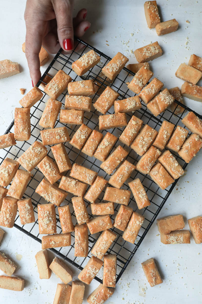 Ine hand holding a wire rack stacked with the baked parmesan cheese cookies.