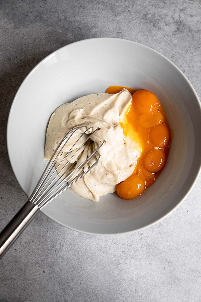 Overhead shot of bechamel sauce and egg yolk in a white bowl