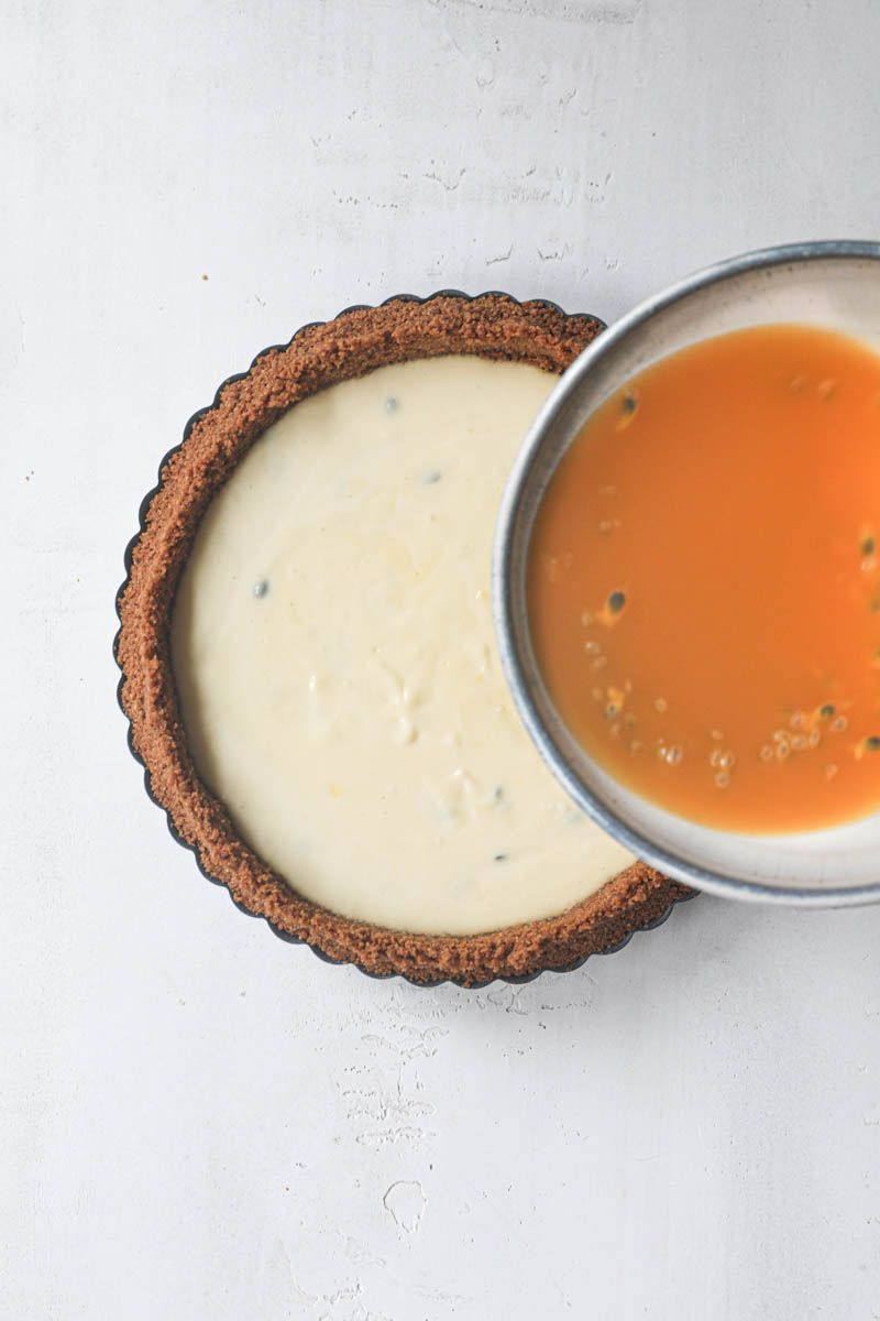 One hand pouring the passion fruit jelly onto the passion fruit cheesecake tart.