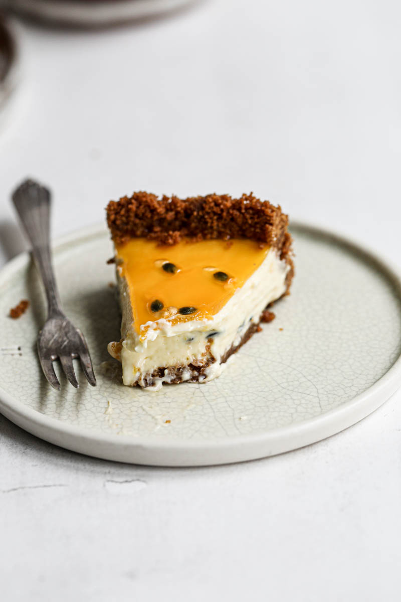 Once slice of passion fruit cheesecake tart on a green plate with a fork on the side.