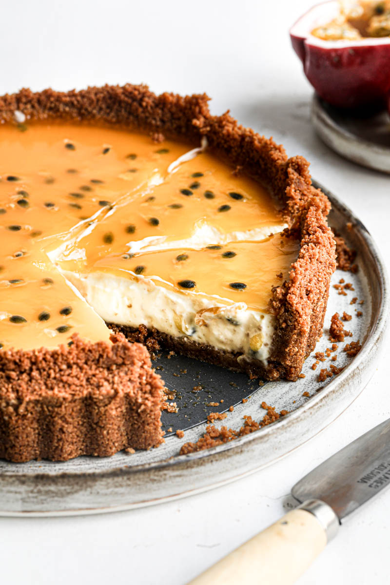 The sliced cheesecake tart as seen from the side on a grey plate with a passion fruit on the side of the frame.