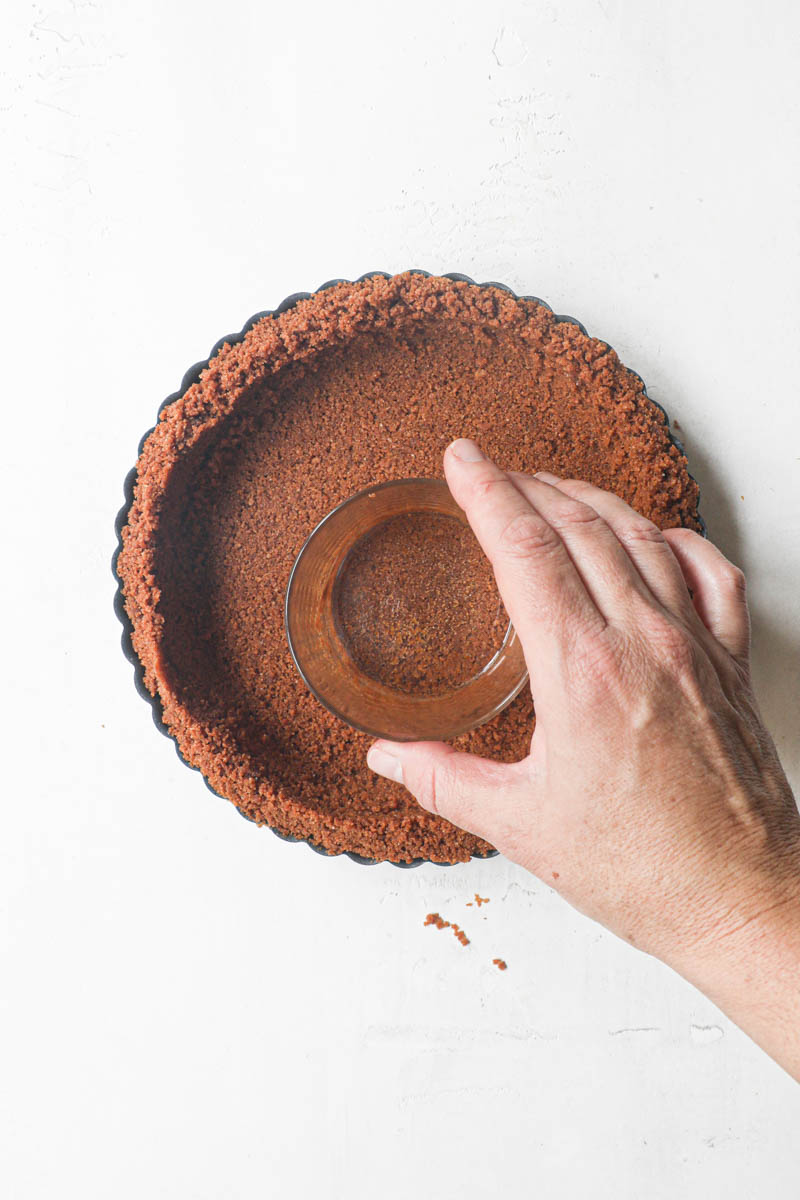 Pne hand pressing the crust onto the tart tin with a glass.