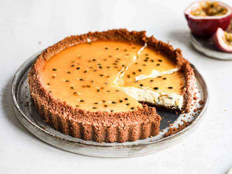 The sliced cheesecake tart as seen from the side on a grey plate with a passion fruit on the side of the frame.