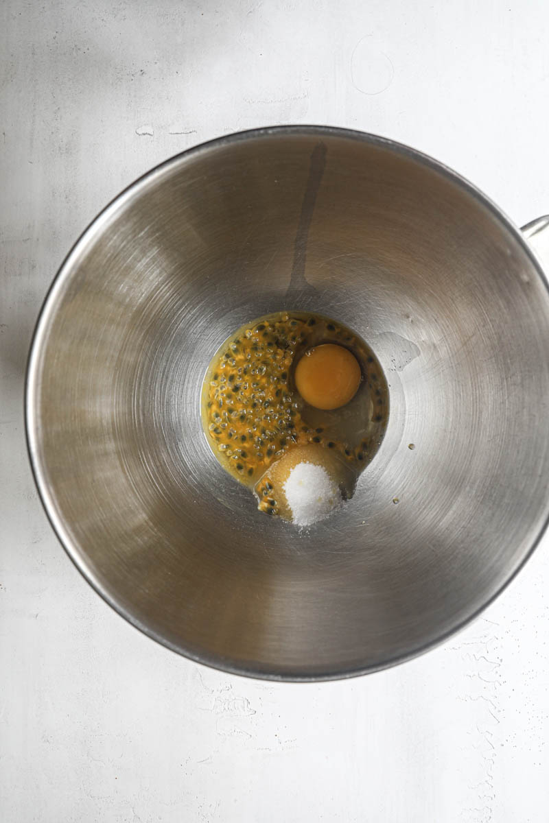 Two egg, the sugar and the passion fruit inside a mixing bowl.