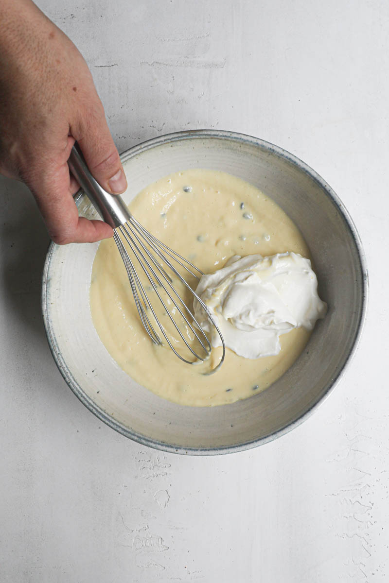 One hand folding the whipped cream into the passion fruit batter.