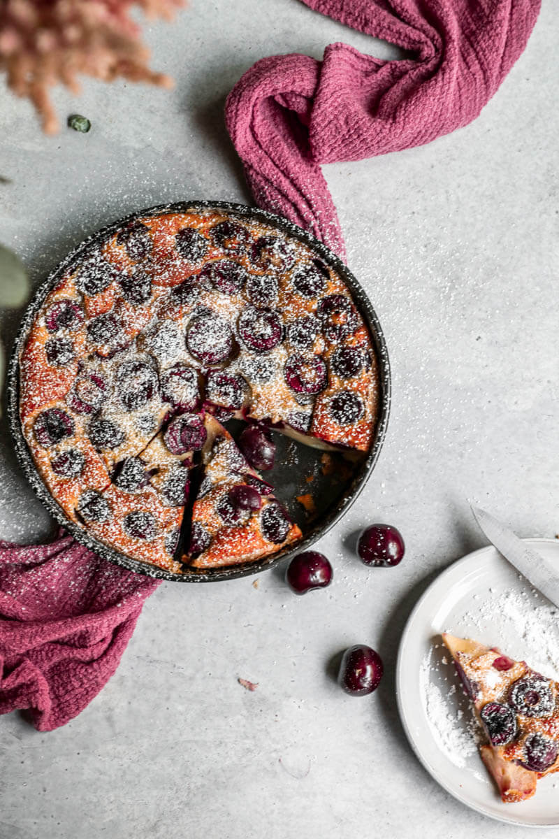 Overhead shot of the baked cherry clafoutis sprinkled with powdered sugar with some sliced portions