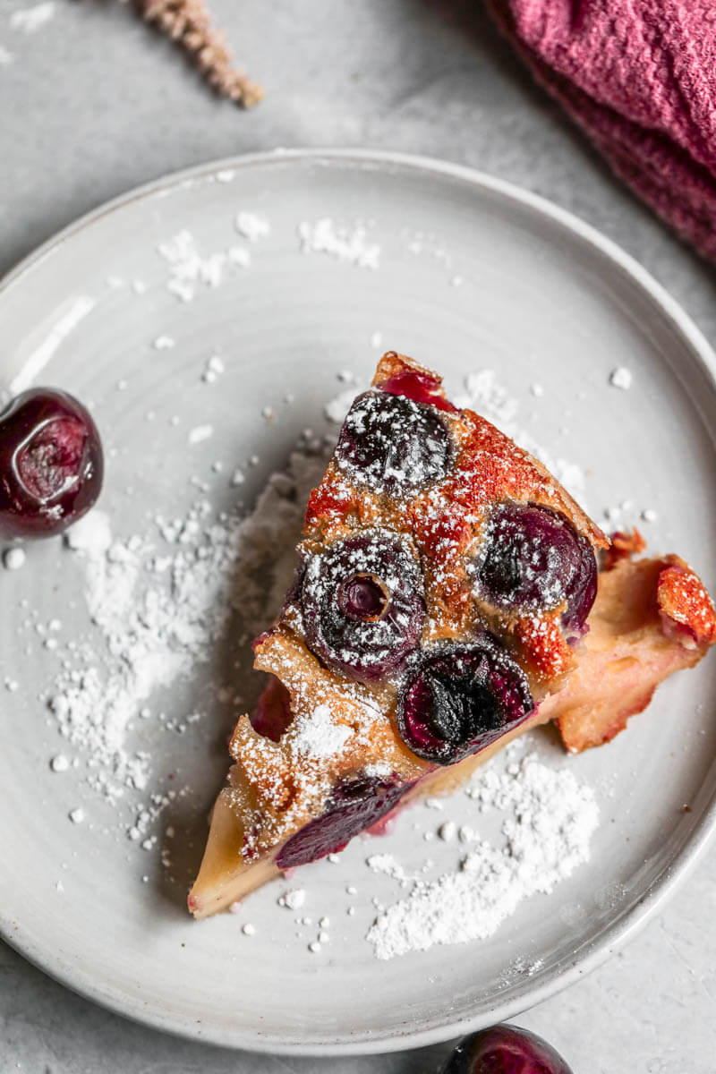 Overhead shot of one slice of cherry clafoutis on a grey plate