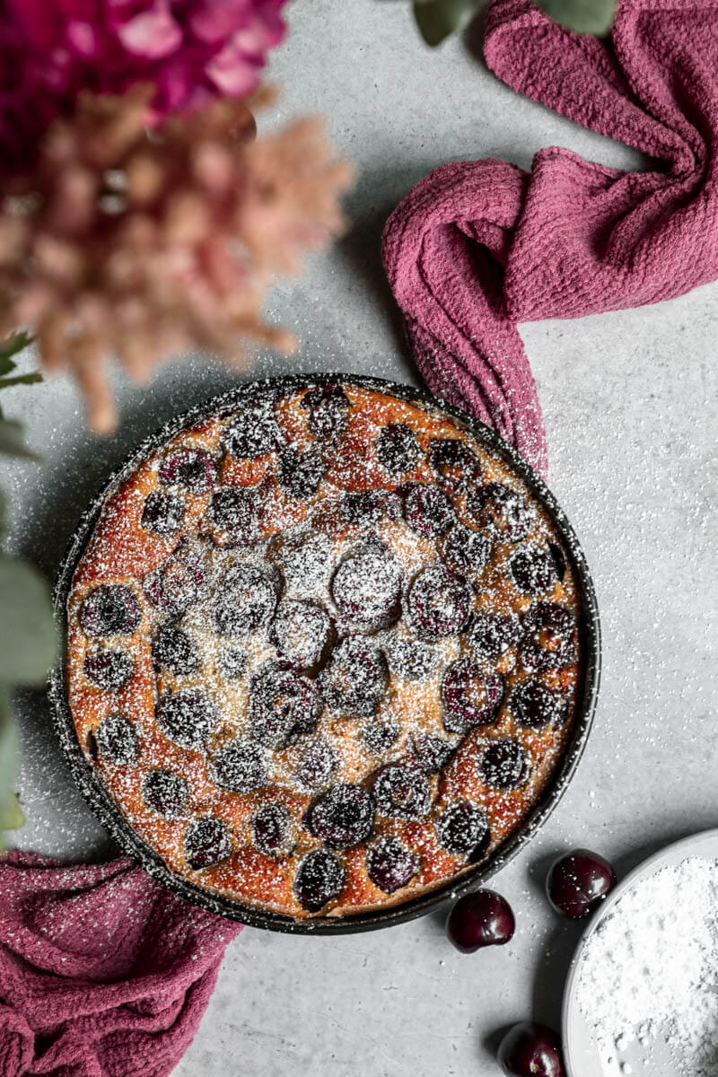 Overhead shot of the baked cherry clafoutis in the baking dish sprinkled with powdered sugar