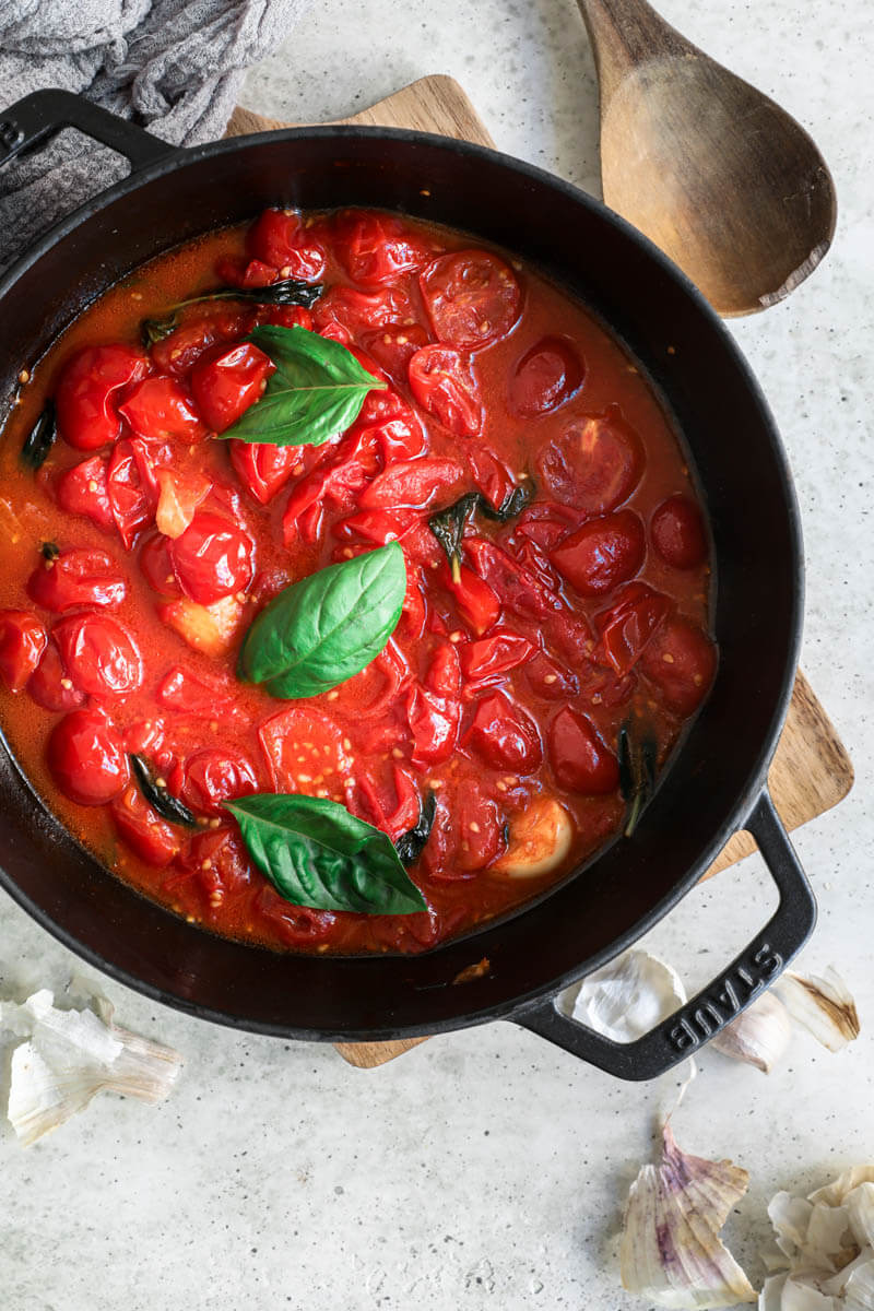 Overhead shot of a black pan with the cherry tomato sauce topped with basil leaves