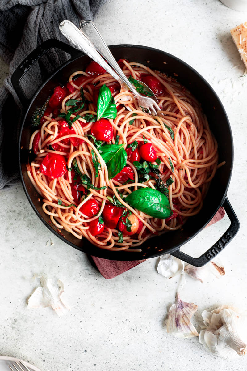 Overhead shot of a black pan filled with pasta and topped with cherry tomato sauce with a fork and a spoon in the corner