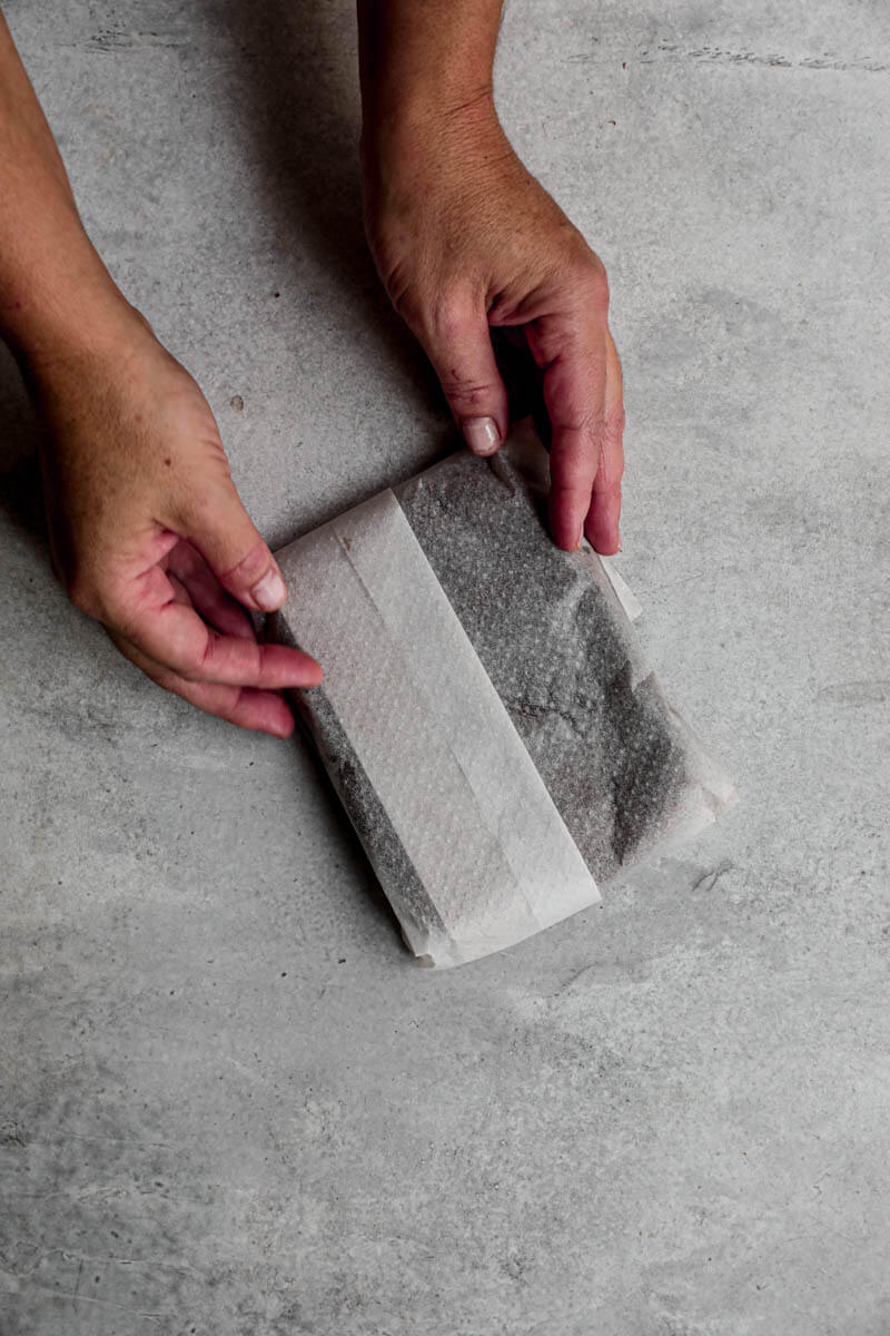 Overhead shot of 2 hands holding the alfajores cookie dough covered in parchment paper